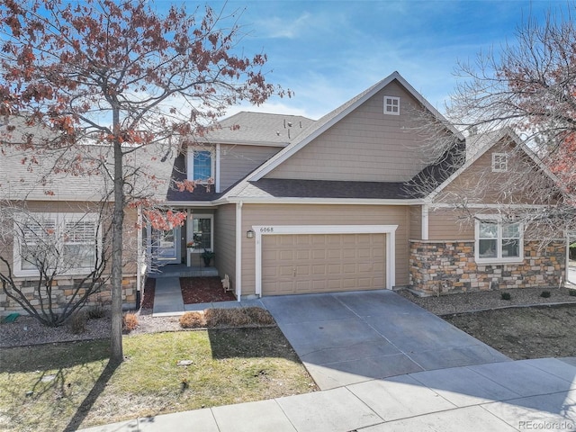 craftsman-style home featuring roof with shingles, driveway, stone siding, and an attached garage