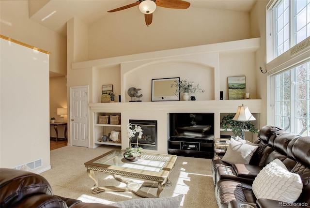 carpeted living room with a glass covered fireplace, visible vents, a high ceiling, and a ceiling fan