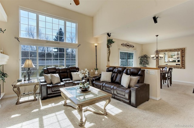 carpeted living area with ceiling fan with notable chandelier, a high ceiling, baseboards, and a healthy amount of sunlight