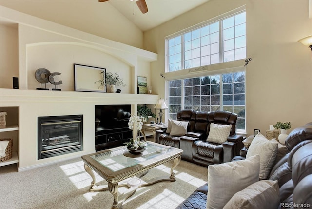 carpeted living room with built in features, high vaulted ceiling, a ceiling fan, and a glass covered fireplace