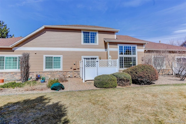 back of property with a yard, stone siding, fence, and a shingled roof