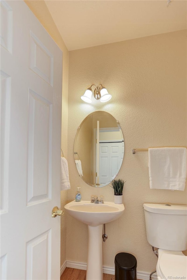 half bath with baseboards, toilet, and wood finished floors