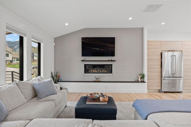 living area featuring a glass covered fireplace, lofted ceiling, recessed lighting, and visible vents