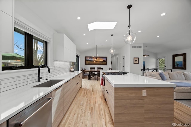 kitchen featuring vaulted ceiling with skylight, modern cabinets, dishwasher, a sink, and white cabinetry
