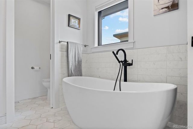 full bath featuring tile walls, tile patterned flooring, a wainscoted wall, toilet, and a soaking tub