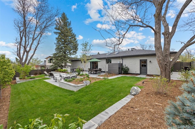 rear view of property with a lawn, brick siding, fence, and a patio area