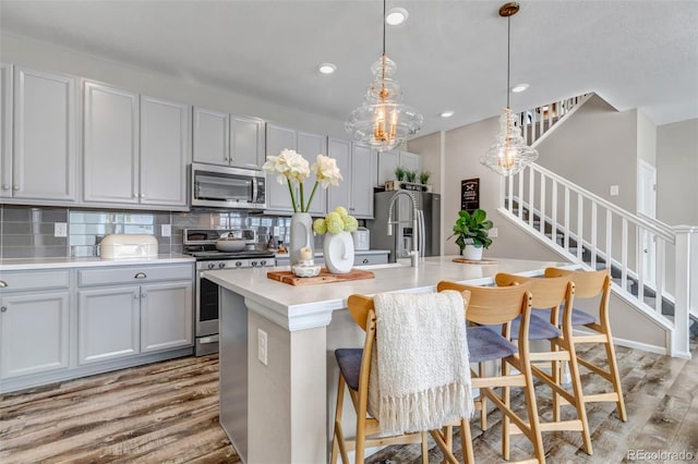 3778 Happyheart Way, Castle Rock, CO 80109 - kitchen with appliances with stainless steel finishes, light wood-type flooring, a center island with sink, light countertops, and backsplash