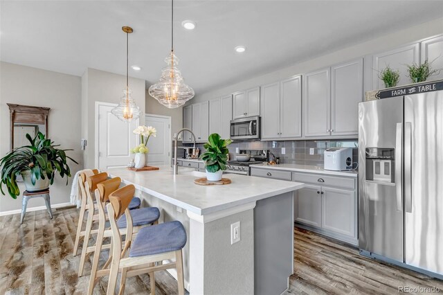 3778 Happyheart Way, Castle Rock, CO 80109 - kitchen with stainless steel appliances, light countertops, light wood-style flooring, a center island with sink, and a breakfast bar area