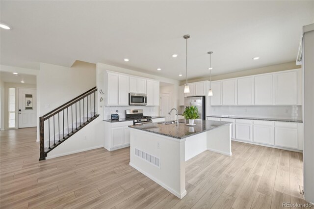 12854 Clearview St, Firestone, CO 80504 - kitchen with stainless steel appliances, light wood finished floors, an island with sink, white cabinets, and recessed lighting