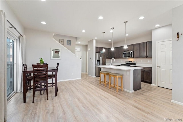 kitchen featuring dark brown cabinetry, appliances with stainless steel finishes, a sink, light wood-style floors, and light countertops