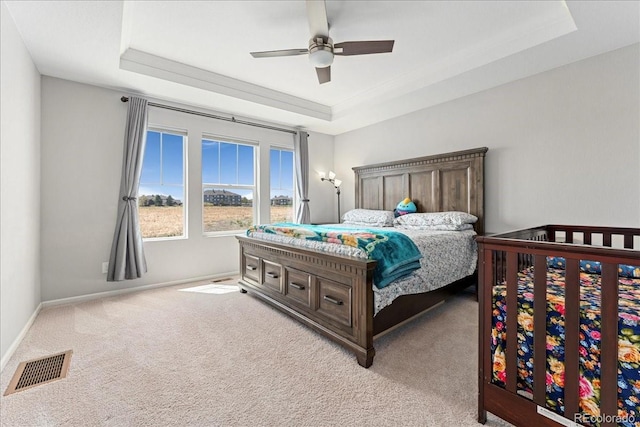 bedroom with carpet flooring, a ceiling fan, baseboards, a tray ceiling, and visible vents