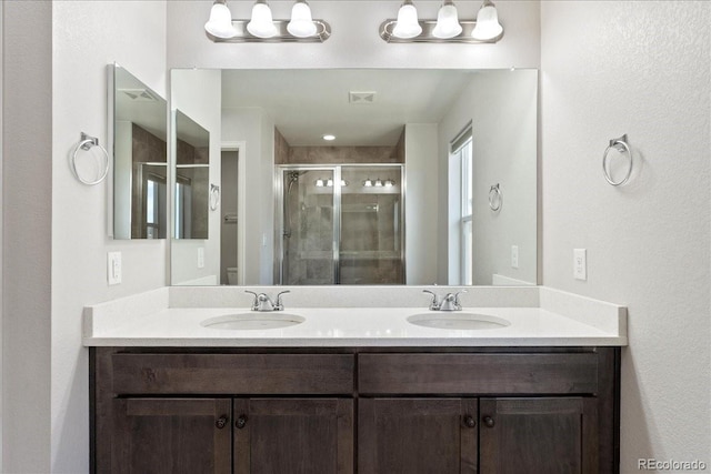 bathroom featuring double vanity, visible vents, a shower stall, and a sink