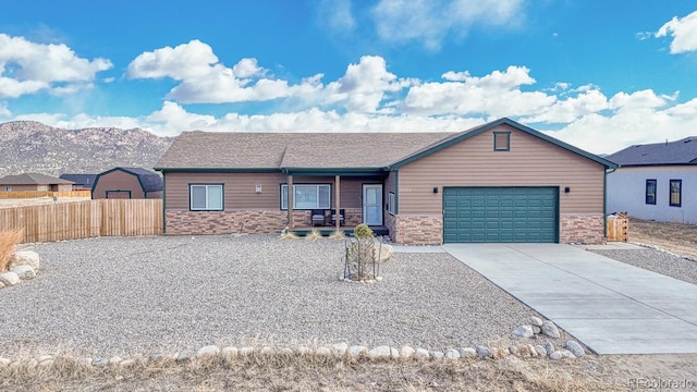 view of front facade featuring an attached garage, a mountain view, fence, stone siding, and concrete driveway