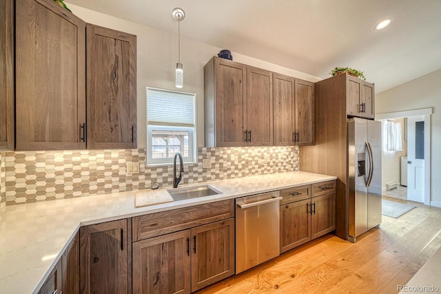 kitchen with decorative backsplash, appliances with stainless steel finishes, vaulted ceiling, light wood-type flooring, and a sink