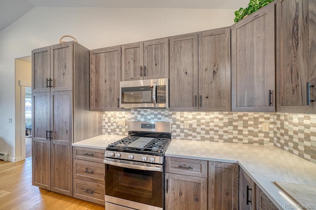 kitchen with vaulted ceiling, stainless steel appliances, light wood finished floors, and backsplash