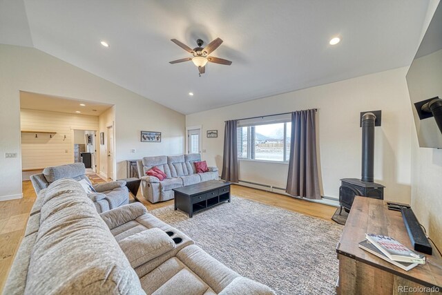 living area featuring ceiling fan, light wood-style flooring, a wood stove, vaulted ceiling, and recessed lighting