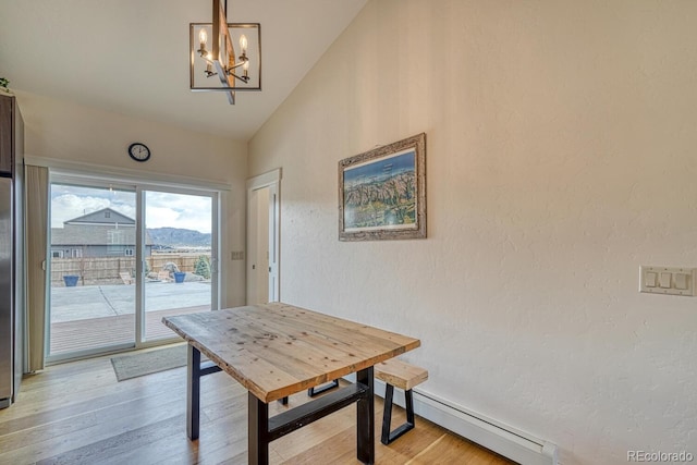 dining room featuring a chandelier, a textured wall, light wood-style flooring, vaulted ceiling, and baseboard heating