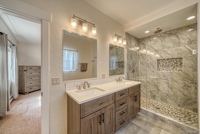 full bathroom featuring double vanity, a textured wall, tiled shower, and a sink