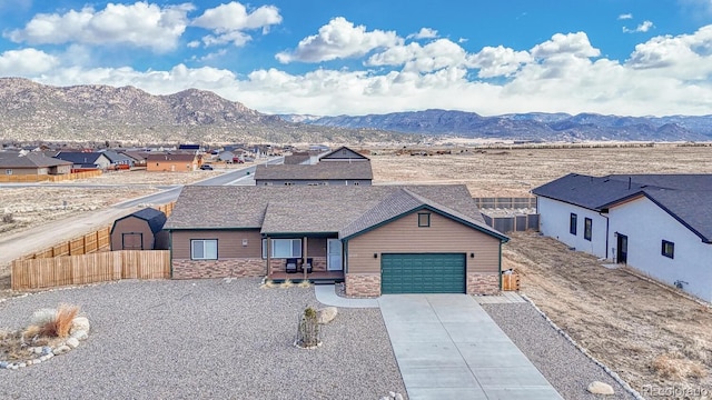 view of front of home featuring stone siding, concrete driveway, fence, and a mountain view