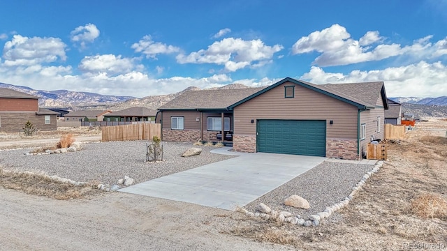 ranch-style house with driveway, a garage, stone siding, fence, and a mountain view