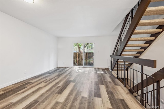 unfurnished living room with stairway, baseboards, and wood finished floors