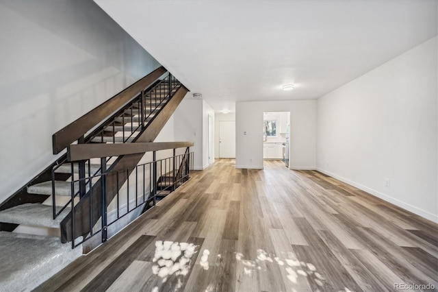 unfurnished living room featuring stairway, wood finished floors, and baseboards