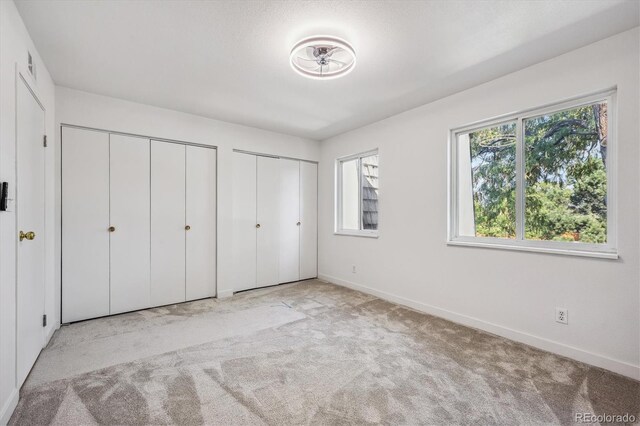 unfurnished bedroom with two closets and light colored carpet