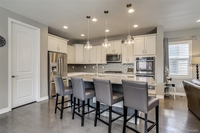 8444 E 55th Pl, Denver, CO 80238 - kitchen with appliances with stainless steel finishes, tasteful backsplash, dark wood-style floors, a kitchen breakfast bar, and recessed lighting