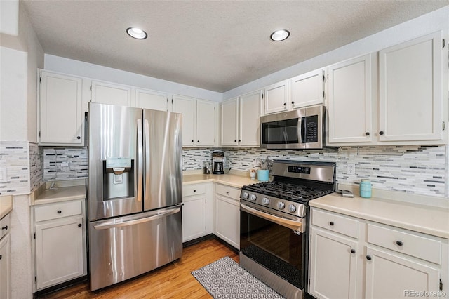 12261 N Holly Way, Brighton, CO 80602 - kitchen with appliances with stainless steel finishes, light countertops, tasteful backsplash, light wood finished floors, and white cabinetry