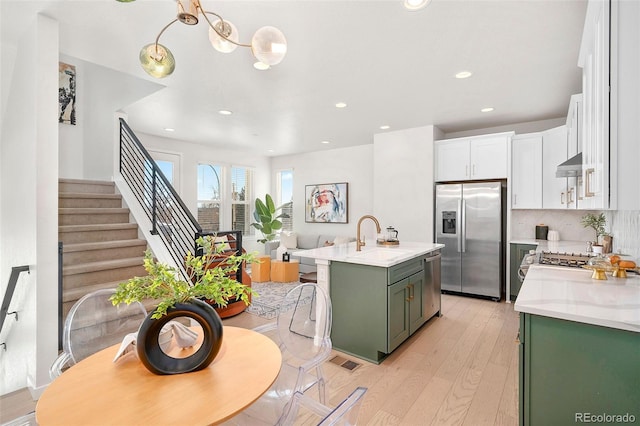 kitchen featuring sink, white cabinetry, green cabinetry, appliances with stainless steel finishes, and an island with sink