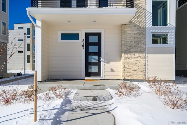 snow covered property entrance featuring a balcony