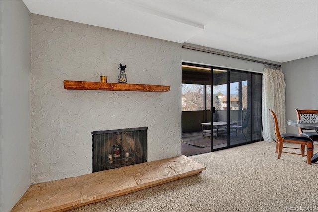 living room with carpet, a fireplace with raised hearth, and a textured wall