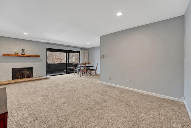 unfurnished living room with carpet floors, baseboards, a fireplace with raised hearth, and recessed lighting