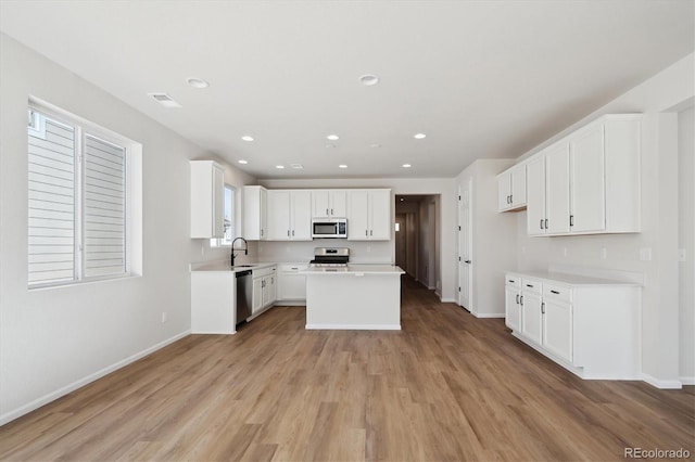 kitchen featuring sink, light hardwood / wood-style flooring, stainless steel appliances, a center island, and white cabinets