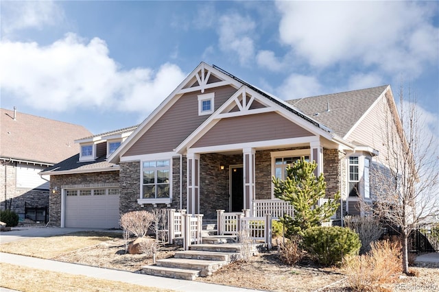 view of front of home featuring an attached garage, covered porch, a shingled roof, concrete driveway, and stone siding