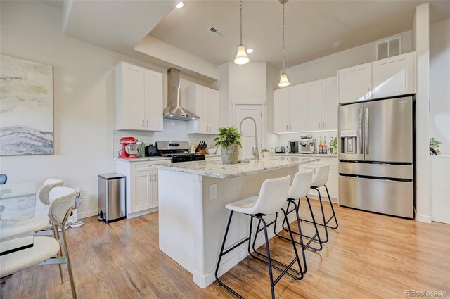 kitchen featuring white cabinets, a center island with sink, wall chimney exhaust hood, and appliances with stainless steel finishes