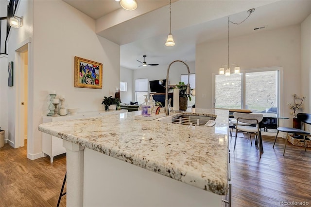 kitchen with light stone counters, ceiling fan with notable chandelier, sink, hardwood / wood-style floors, and hanging light fixtures