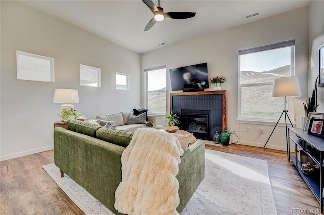 living room featuring ceiling fan, light hardwood / wood-style flooring, a wealth of natural light, and a brick fireplace