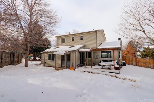 snow covered rear of property with entry steps, a chimney, and a fenced backyard