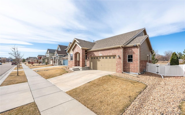 view of front facade with fence, a residential view, roof with shingles, concrete driveway, and brick siding