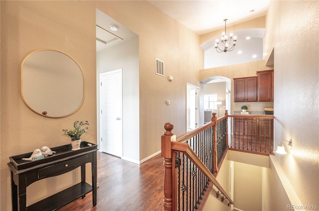 corridor with dark wood-style floors, baseboards, arched walkways, a towering ceiling, and an upstairs landing