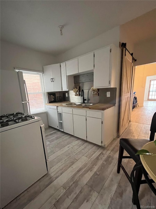 kitchen with sink, light wood-type flooring, white cabinets, a barn door, and white appliances