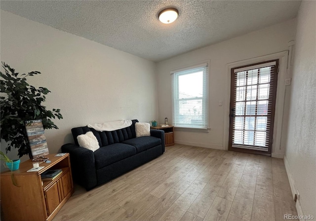 living room with light wood-style flooring, a textured ceiling, baseboards, and a textured wall