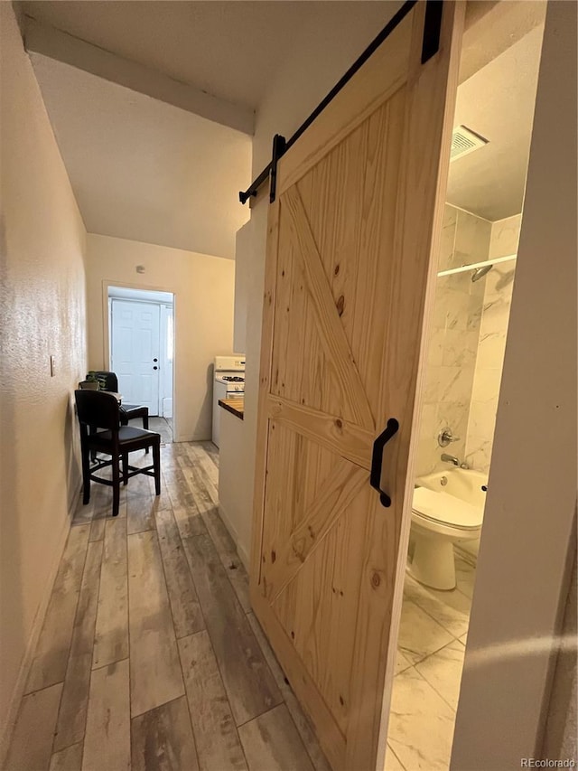 hallway featuring a barn door, baseboards, and light wood finished floors