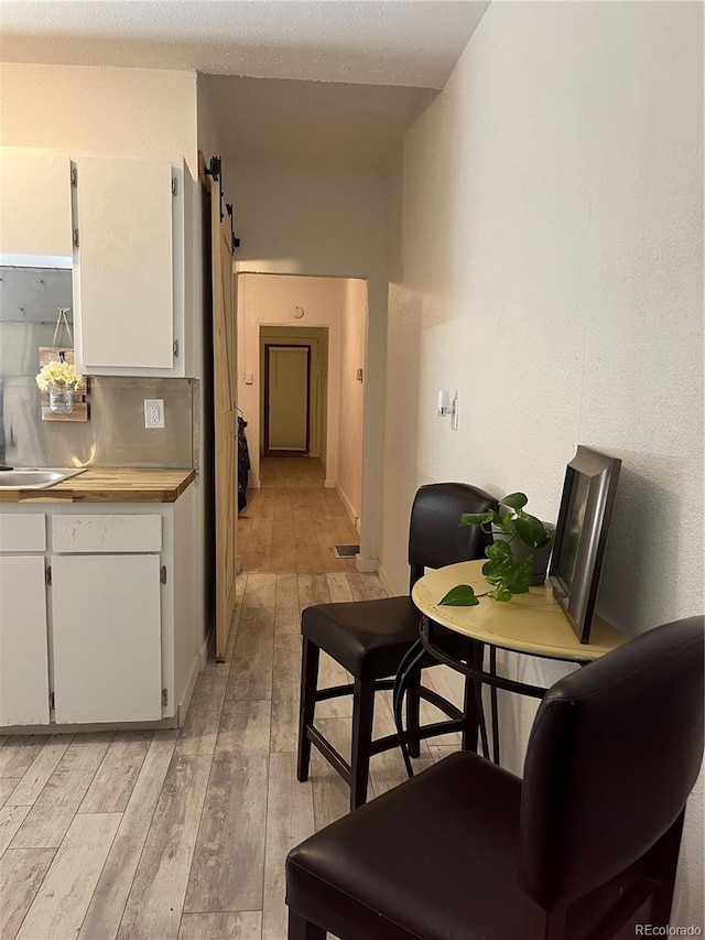 kitchen featuring a barn door, light wood-type flooring, light countertops, baseboards, and white cabinetry