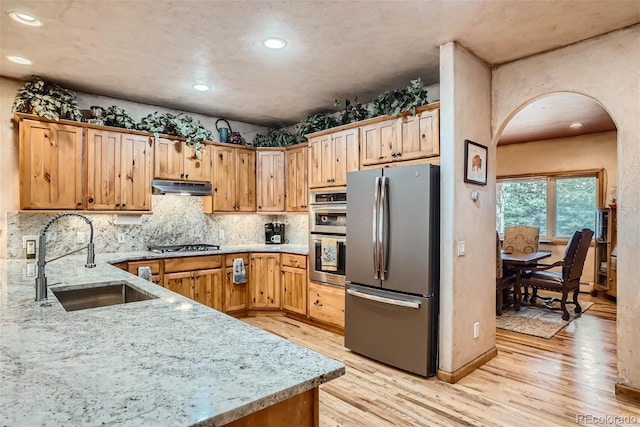 1361 Bross Ct, Evergreen, CO 80439 - kitchen featuring stainless steel appliances, under cabinet range hood, arched walkways, light wood-type flooring, and light stone counters