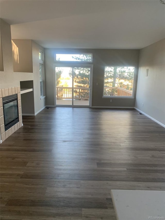 unfurnished living room with dark wood-type flooring and a tiled fireplace