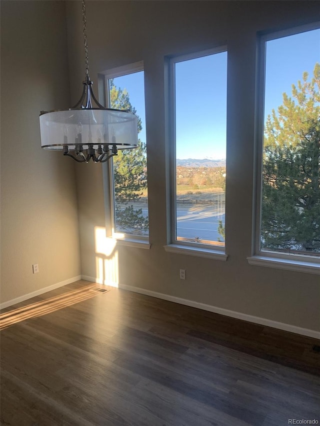 unfurnished dining area with a healthy amount of sunlight, an inviting chandelier, and dark wood-type flooring