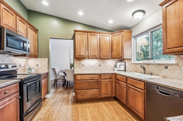 kitchen featuring light wood finished floors, lofted ceiling, appliances with stainless steel finishes, a sink, and backsplash