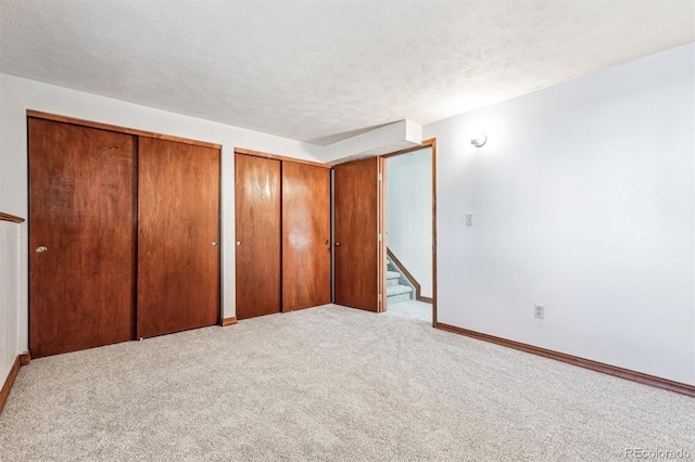 unfurnished bedroom with carpet floors, baseboards, a textured ceiling, and multiple closets